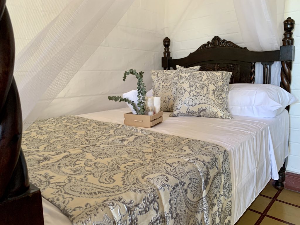Dark wooden bed with mosquito net, light green and cream patterned bedding and box of toiletries